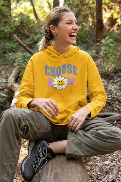 A laughing woman wearing a yellow unisex graphic hoodie with text 'Choose Joy', featuring a large flower with smiley face in the middle