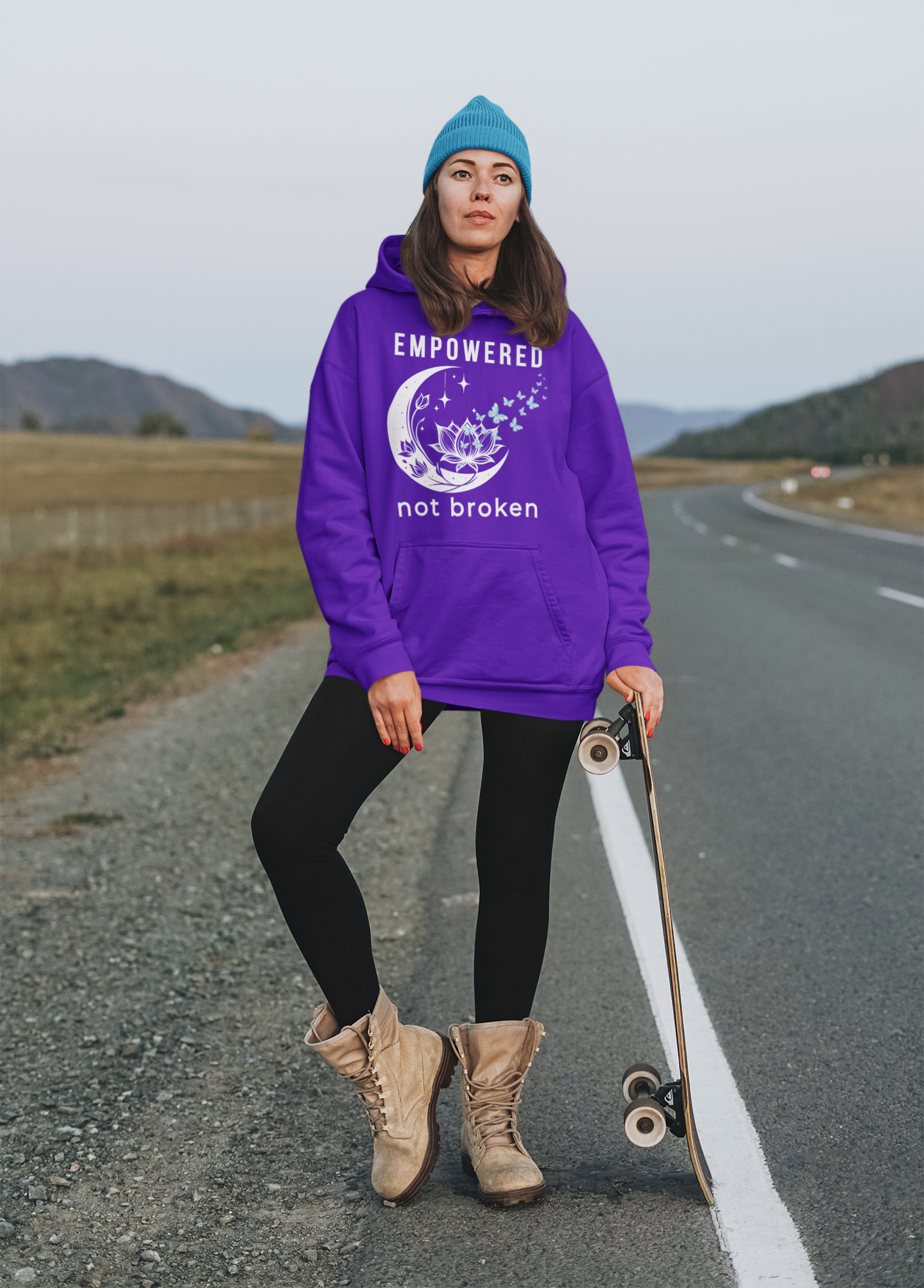 a woman wearing a purple unisex hoodie with text 'empowered not broken', featuring a moon and lotus with little flying butterflies