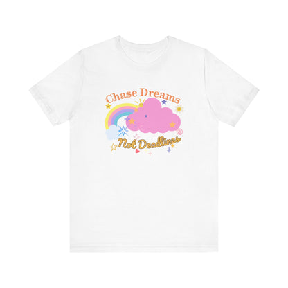 A white unisex graphic t-shirt with the phrase 'Chase Dreams, Not Deadlines' in bold lettering, featuring a rainbow and soft pink cloud