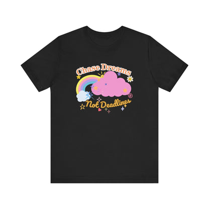 A black unisex graphic t-shirt with the phrase 'Chase Dreams, Not Deadlines' in bold lettering, featuring a rainbow and soft pink cloud