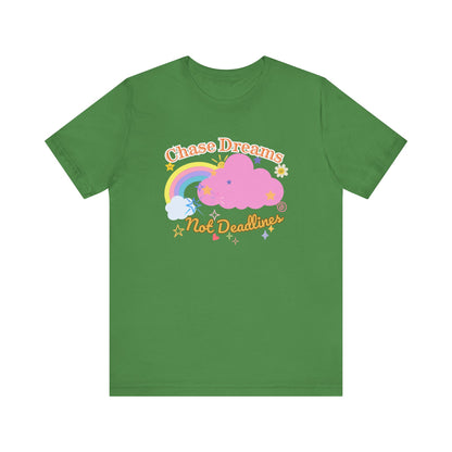 A green unisex graphic t-shirt with the phrase 'Chase Dreams, Not Deadlines' in bold lettering, featuring a rainbow and soft pink cloud