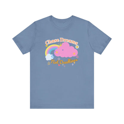 A steel blue unisex graphic t-shirt with the phrase 'Chase Dreams, Not Deadlines' in bold lettering, featuring a rainbow and soft pink cloud