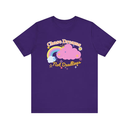 A purple unisex graphic t-shirt with the phrase 'Chase Dreams, Not Deadlines' in bold lettering, featuring a rainbow and soft pink cloud