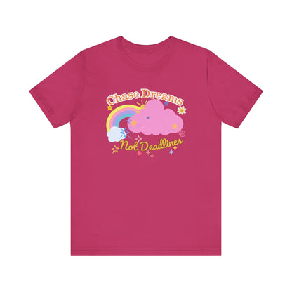 A berry red unisex graphic t-shirt with the phrase 'Chase Dreams, Not Deadlines' in bold lettering, featuring a rainbow and soft pink cloud